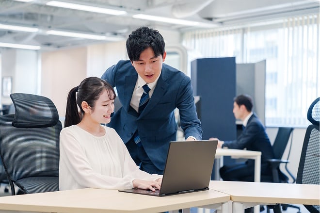 ノートパソコンをしている女性とその横でパソコンを指差している男性